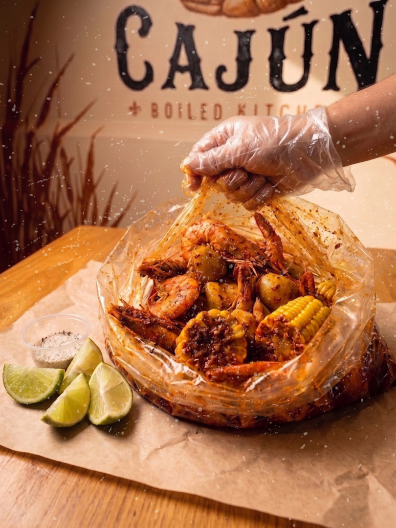 Bolsa de camarones cajún abierta sobre la mesa, con papa, elote y limones